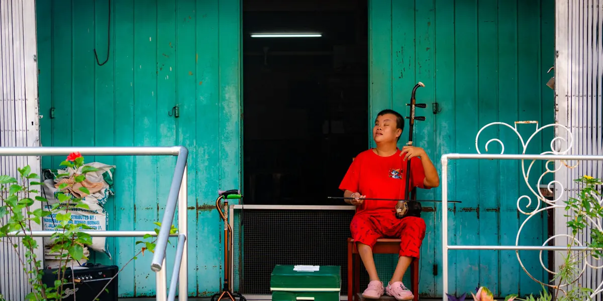 A musician dressed in red playing the erhu in front of turquoise doors