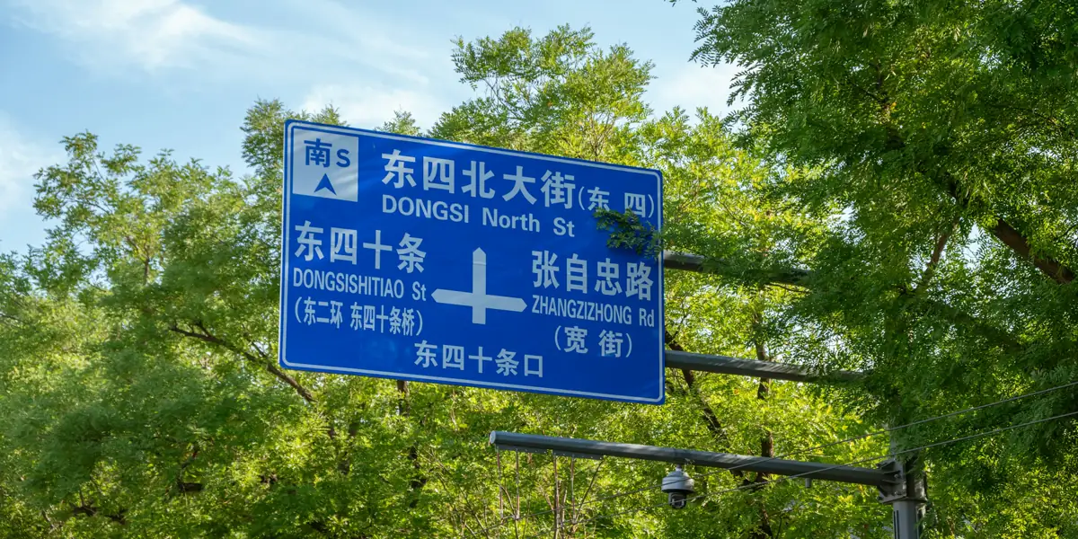 A blue Beijing road sign with street names in Chinese characters and pinyin