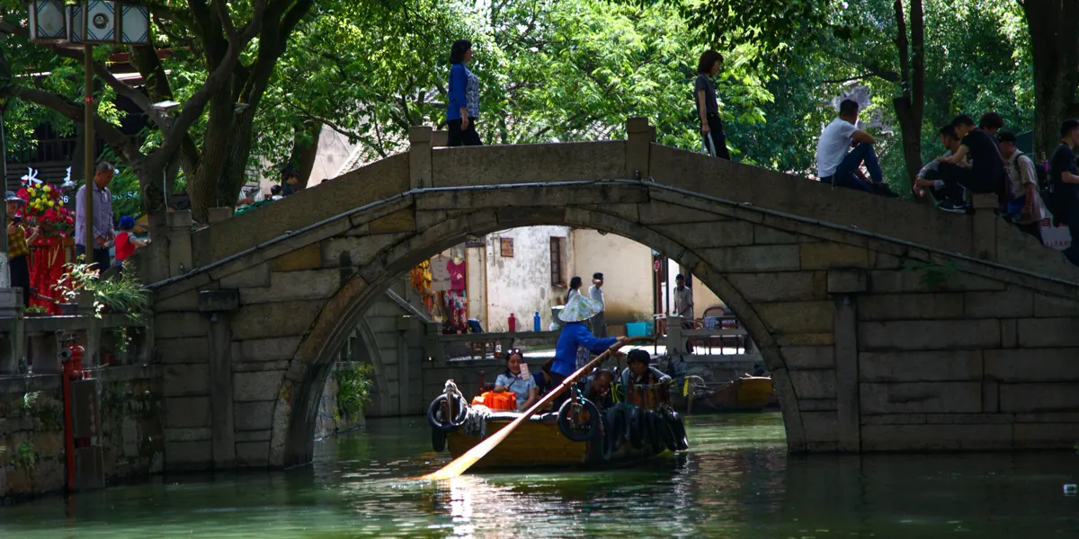 A stone arch bridge over a canal in Tongli water town, with a boat passing underneath
