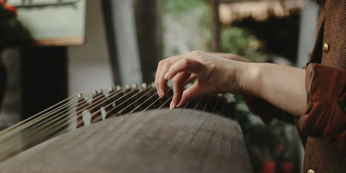 A hand playing the strings of a guzheng, a traditional Chinese zither